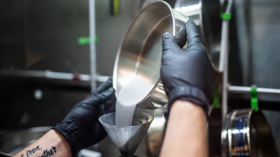Sandia National Laboratories technologist Levi Van Bastian fills a hopper with raw material to print on the Laser Engineered Net Shaping machine. What appears to be a liquid is powdered metal.