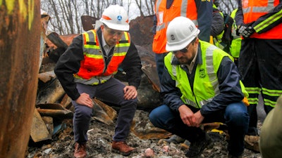 Transportation Secretary Pete Buttigieg, left, and Tristan Brown, deputy administrator of the Pipeline and Hazardous Materials Safety Administration, crouch down to look at part of a burned traincar, Thursday, Feb. 23, 2023, in East Palestine, Ohio, at the site of a Norfolk Southern train derailment.