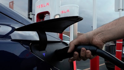 A motorist charges his electric vehicle at a Tesla Supercharger station in Detroit, Wednesday, Nov. 16, 2022. About half of U.S. adults say they are not likely to go electric when it comes time to buy a new vehicle, a new poll by The Associated Press-NORC Center for Public Affairs Research and the Energy Policy Institute at the University of Chicago shows.