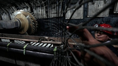 A miner pulls back the wire fence near the shearer at the mining face of Xiaobaodang Coal Mine near the city of Shenmu in northwestern China's Shaanxi province on Wednesday, April 26, 2023.