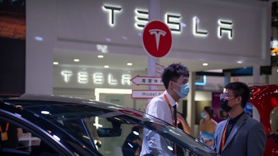 Staff members talk near vehicles at a display for automaker Tesla at the China International Fair for Trade in Services (CIFTIS) in Beijing on Sept. 2, 2022.