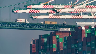 Transportation trucks cross the Vincent Thomas Bridge over the main channel as shipping containers are seen stacked on the Evergreen terminal at the Port of Los Angeles in San Pedro, Calif., Nov. 30, 2021. The union for thousands of West Coast dockworkers has reached a tentative agreement on a new contract, it was announced Wednesday, June 14, 2023, after more than a year of negotiations and several work disruptions that snarled shipping traffic at some of the largest ports.