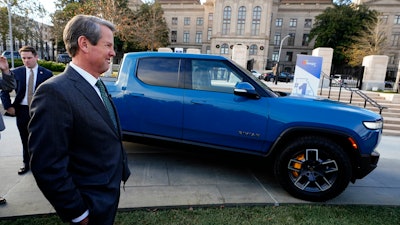 Gov. Brian Kemp smiles as he stands next to a Rivian electric truck during a ceremony to announce that the electric truck maker plans to build a $5 billion battery and assembly plant east of Atlanta projected to employ 7,500 workers, Thursday, Dec. 16, 2021, in Atlanta.