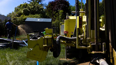 A Dandelion Energy employee sprays excess groundwater back on the lawn during installation of a geothermal heat pump system at a home in White Plains, N.Y., Monday, May 8, 2023. A water-filled loop is installed several hundred feet deep in the yard to either carry heat away from or into the house depending on season.