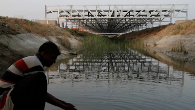 A worker washes his hands as installed solar panels are visible atop the Narmada canal at Chandrasan village, outside of Ahmadabad, India, Feb. 16, 2012.