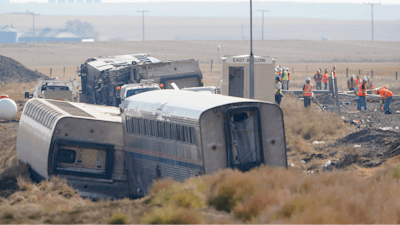 Workers stand near train tracks, Sept. 27, 2021, next to overturned cars from an Amtrak train that derailed near Joplin, Mont.