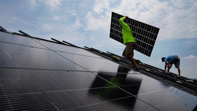 Nicholas Hartnett, owner of Pure Power Solar, carries a panel as he and Brian Hoeppner, right, install a solar array on the roof of a home in Frankfort, Ky., Monday, July 17, 2023.