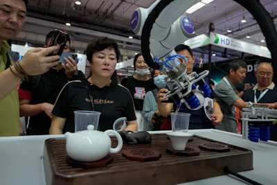 Visitors look at a robotic arm performs a Chinese tea serving during the annual World Robot Conference at the Etrong International Exhibition and Convention Center on the outskirts of Beijing, Thursday, Aug. 17, 2023.