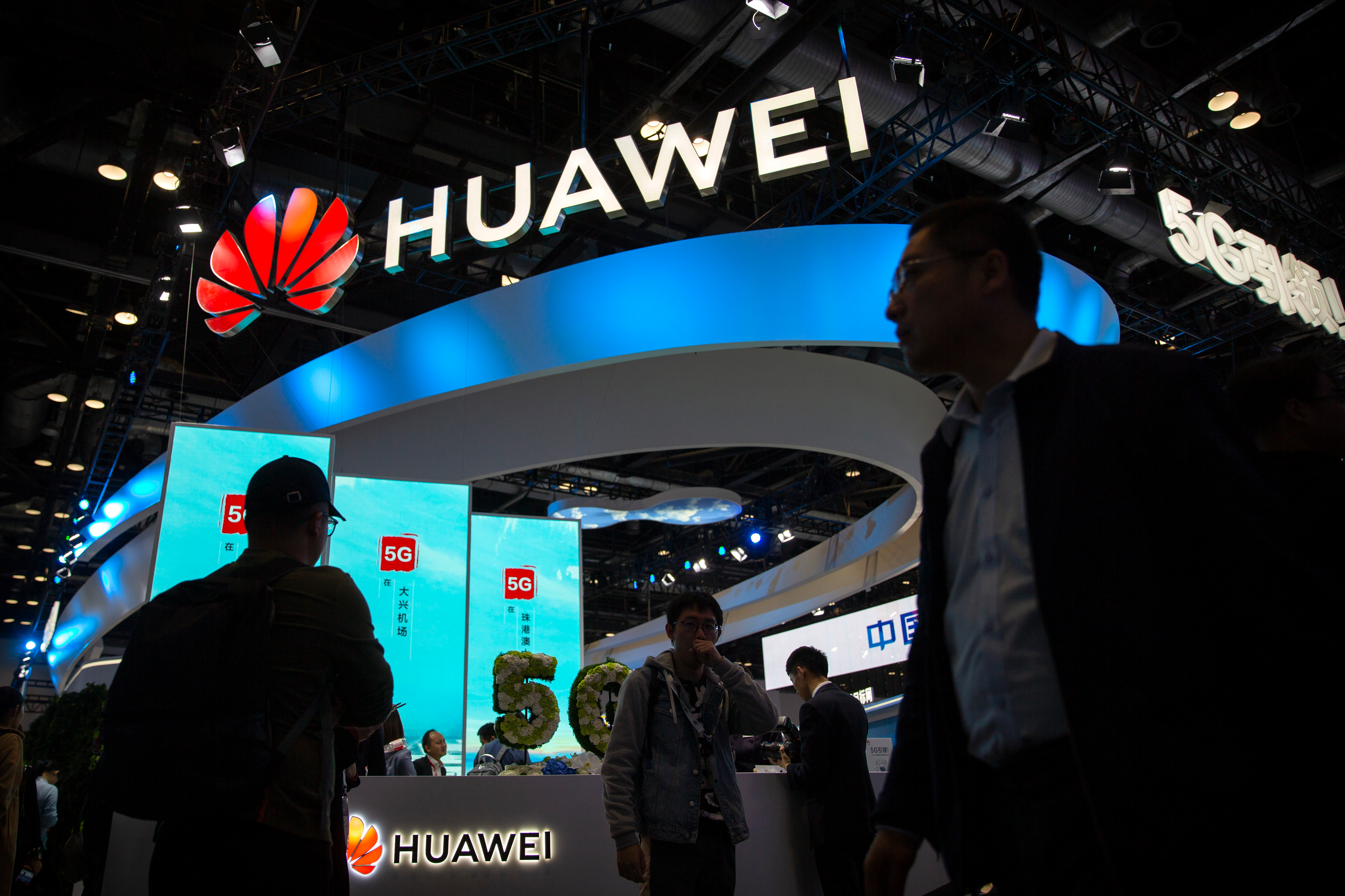 Attendees walk past a display for 5G services from Chinese technology firm Huawei at the PT Expo in Beijing, on Oct. 31, 2019.