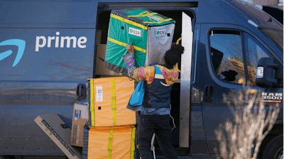 An Amazon Prime delivery person struggles with packages while making a stop at a high-rise apartment building on Tuesday, Nov. 28, 2023, in Denver.