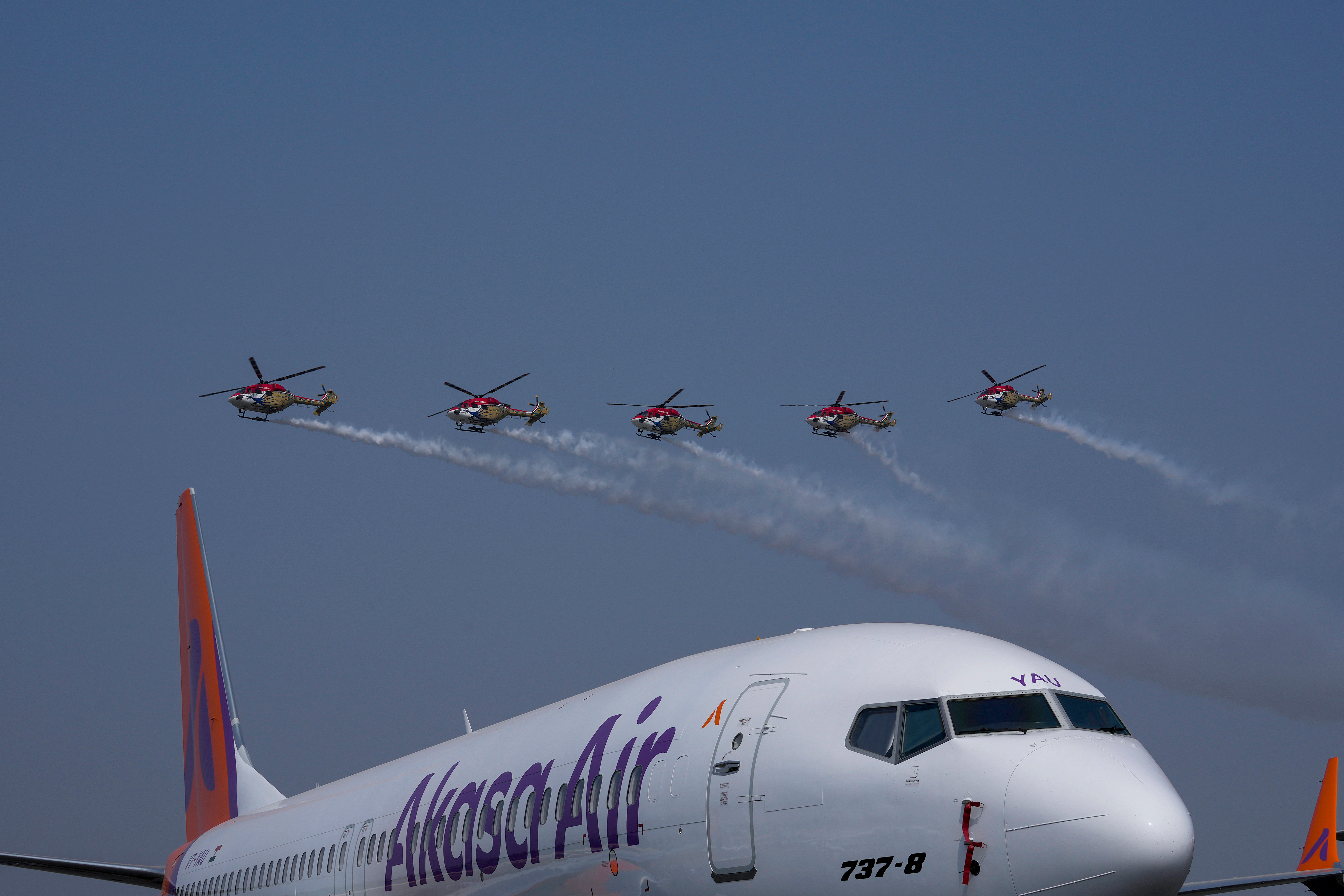 Akasa Air's 737-8 aircraft is seen in foreground as Indian Air Force Sarang helicopters perform an aerobatic display during the 'Wings India 2024,' a biennial aviation event at Begumpet airport in Hyderabad, India, Thursday, Jan. 18, 2024.