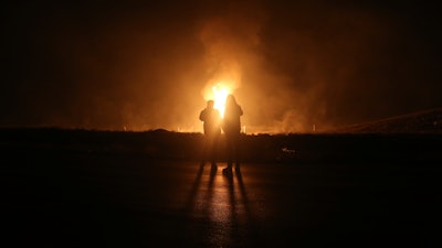 Two men look at flames after a natural gas pipeline explodes outside the city of Boroujen in the western Chaharmahal and Bakhtiari province, Iran, in early Wednesday, Feb. 14, 2024.