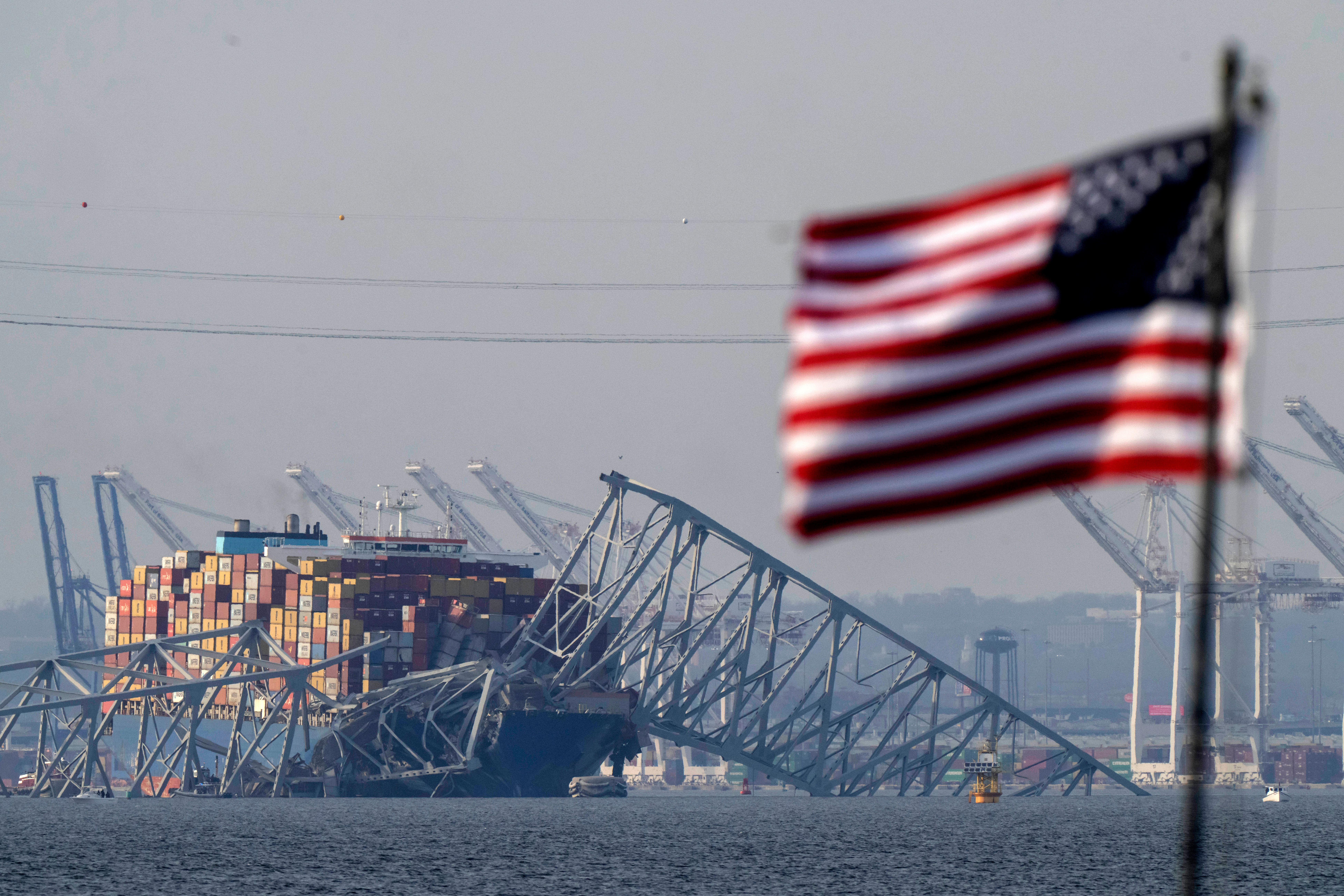 An American flag flies on a moored boat as the container ship Dali rests against wreckage of the Francis Scott Key Bridge, Tuesday, March 26, 2024, as seen from Pasadena, Md.