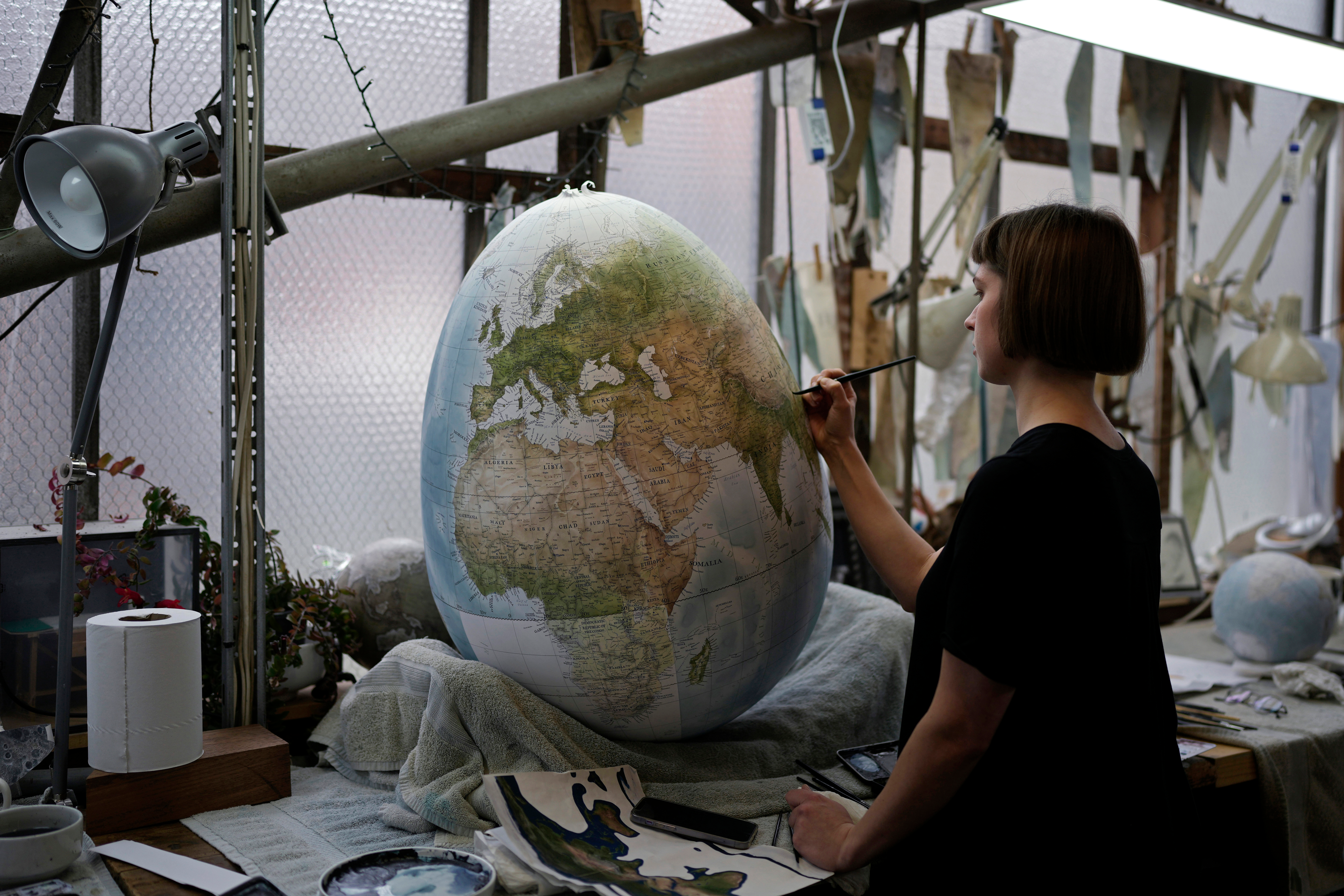 An artist paints a globe at a studio in London, Tuesday, Feb. 27, 2024.
