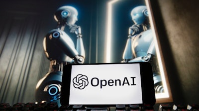 The OpenAI logo is seen displayed on a cell phone with an image on a computer monitor generated by ChatGPT's Dall-E text-to-image model, Friday, Dec. 8, 2023, in Boston.