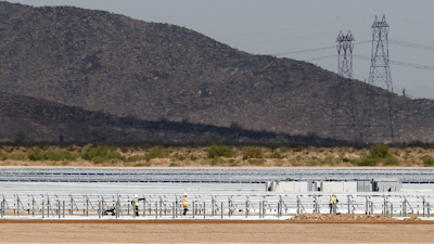 Workers continue to build rows of solar panels at a Mesquite Solar 1 facility under construction in Arlington, Ariz.