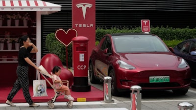 A woman pushes a child past a Red Tesla vehicle at a charging station in Beijing.