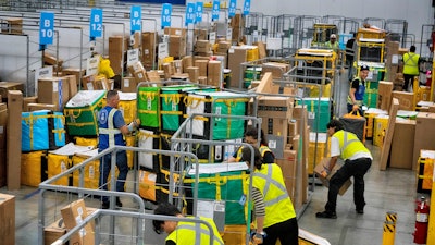 Amazon employees load packages on carts at an Amazon DAX7 delivery station, July 16, 2024, South Gate, Calif.