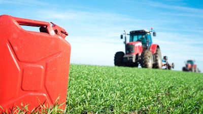 A gas can sits before a tractor in a field.