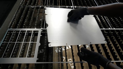 A worker lifts a steel sheet after cutting it in a specific design at a factory in a suburb of Bengaluru, India, Feb. 27, 2025.
