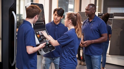An engineer shows apprentices how to use a CNC machine.