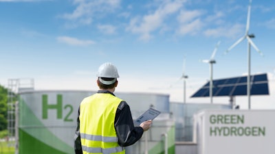 Worker in safety vest inspecting green hydrogen production facility with solar and wind energy.
