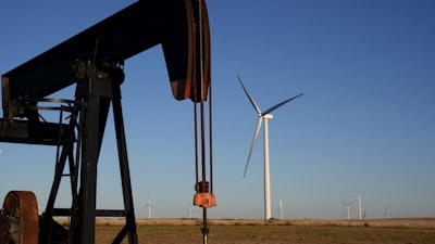 Pumpjacks operate in the foreground while a wind turbines at the Buckeye Wind Energy wind farm rise in the distance Monday, Sept. 30, 2024, near Hays, Kan.
