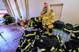 Firefighter Christopher Harrington stands next to the station's old turnout gear, while wearing recently issued non-PFAS turnout gear, at Fire Station 4 on July 3, 2025, in East Providence, R.I.