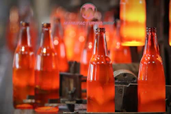 Orange glass bottles on industrial manufacturing conveyor line with warm lighting