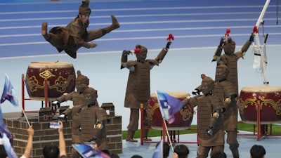 A human performer leaps above robots dressed like terracotta warriors during the opening ceremony of The World Humanoid Robot Games held in Beijing, China, Thursday, Aug. 14, 2025.