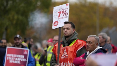 A worker holds a sign reading 'investing instead of saving' during a nationwide warning strike of the union IG Metal at the car maker FORD factory in Cologne, Germany, Germany, Oct. 29, 2024.