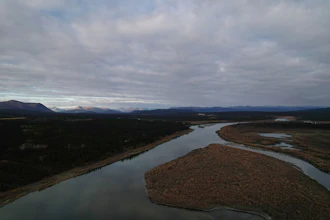 Winding river through forested valley with distant mountain ranges under cloudy sky
