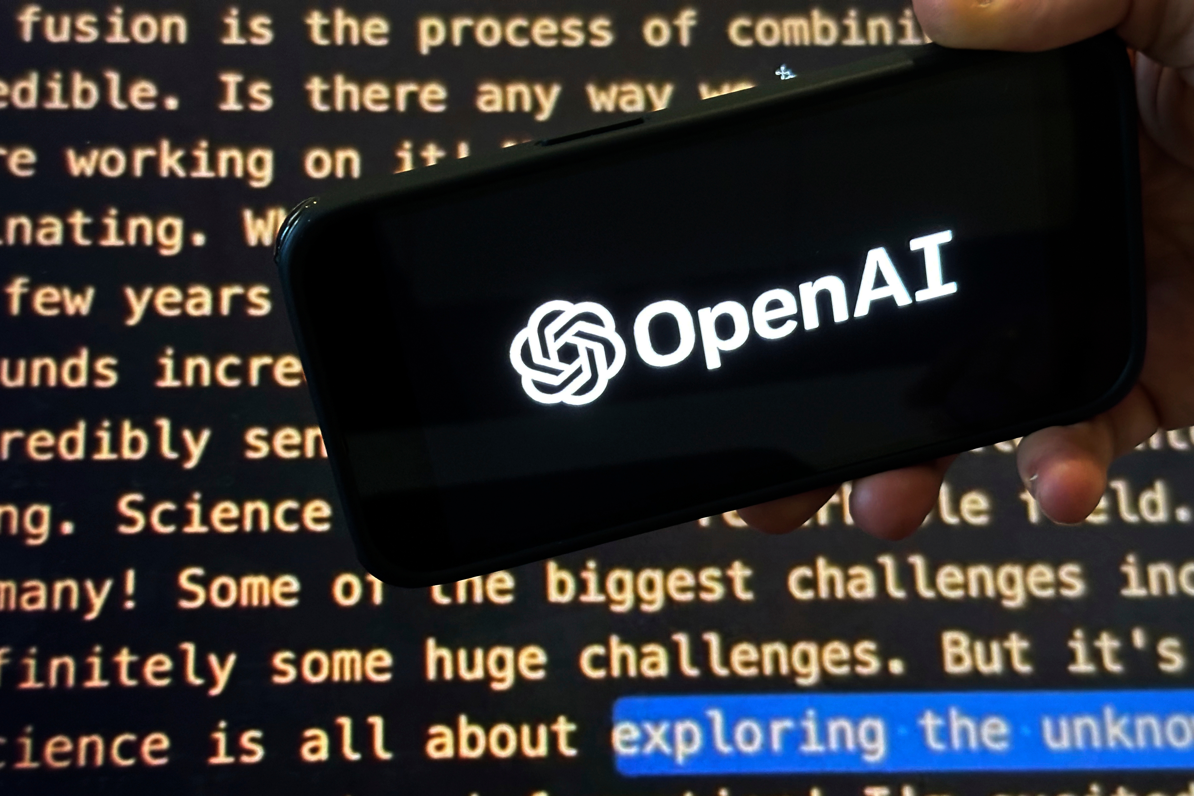 The OpenAI logo appears on a mobile phone in front of a screen showing part of the company website in this photo taken on Nov. 21, 2023 in New York.