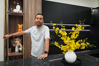 Man standing in modern kitchen with yellow orchids and decorative shelving