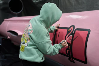 Person in green hoodie painting flamingo silhouette on pink background