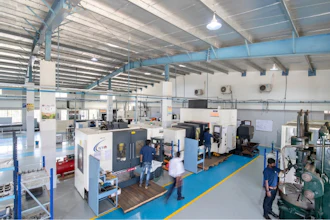 Industrial manufacturing facility with CNC machines and workers on blue-lined floor