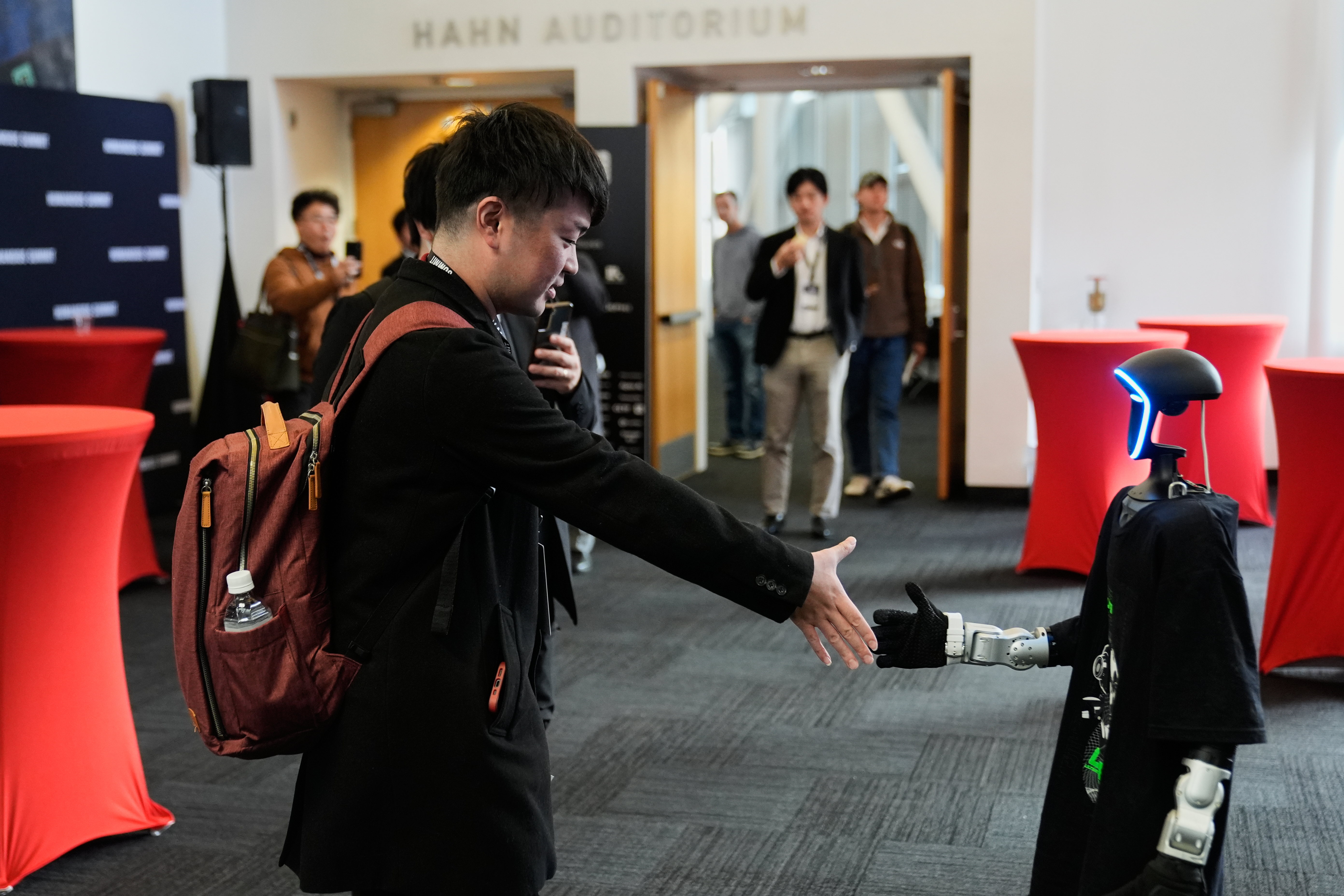 Kochi Sato, left, shakes hands with a humanoid robot during the Humanoids Summit, Thursday, Dec. 11, 2025, in Mountain View, Calif.