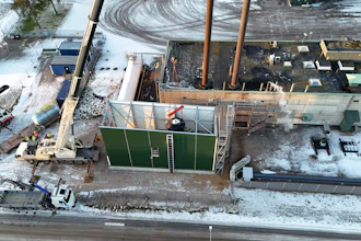 Aerial winter construction site with crane, trucks, and green temporary walls