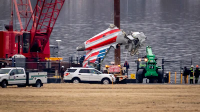 A crane offloads a piece of wreckage from a salvage vessel onto a flatbed truck, near the wreckage site in the Potomac River of a mid-air collision between an American Airlines jet and a Black Hawk helicopter, at Ronald Reagan Washington National Airport, Feb. 5, 2025, in Arlington, Va.