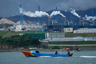 Colorful fishing boat near industrial plant with smoking chimneys on coastal landscape