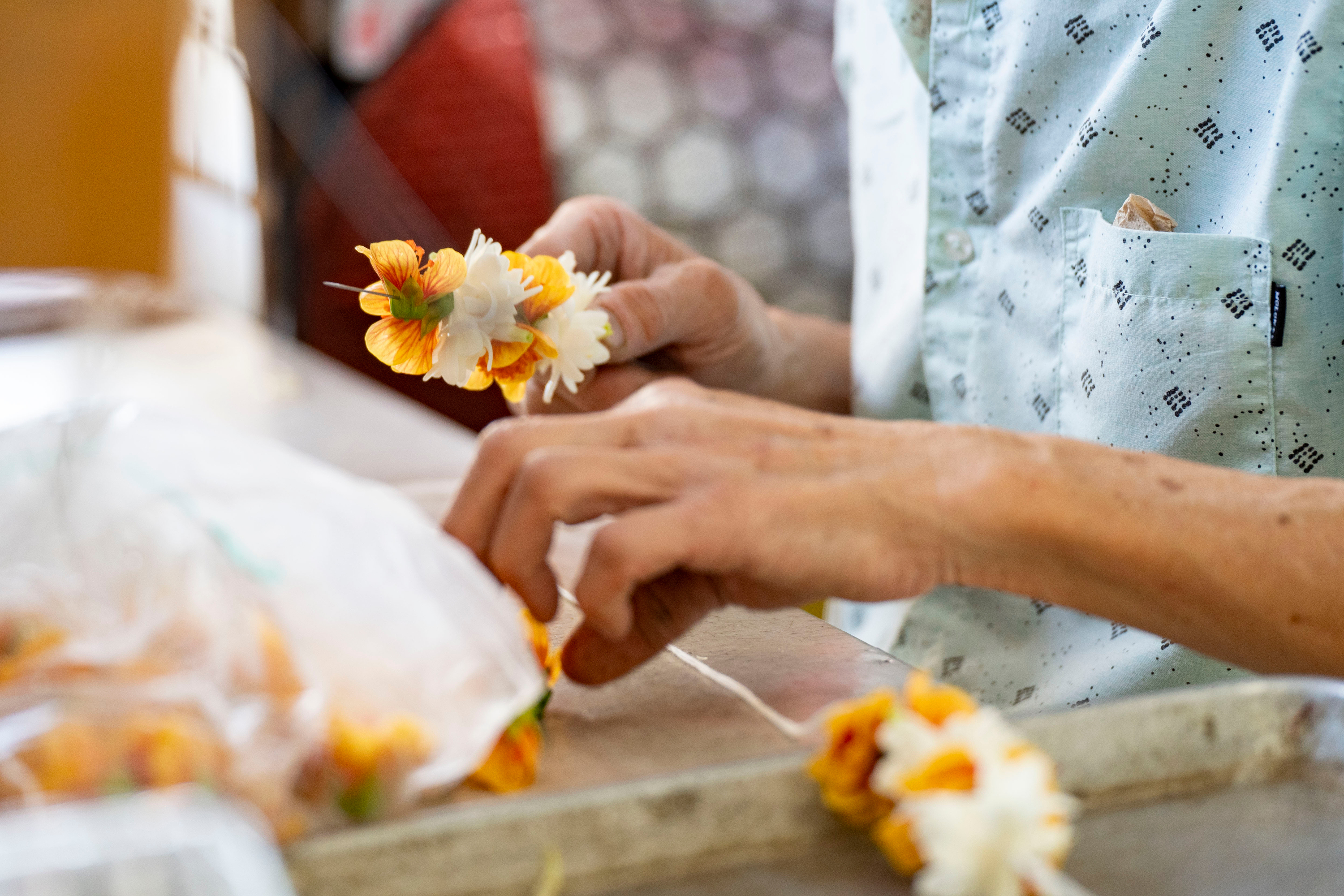 Sam Say, owner of M.P. Lei Shop, strings flowers to make a lei at his shop in Chinatown, Thursday, Feb. 26, 2026, in Honolulu.