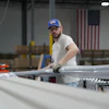 A worker lifts an aluminum beam on the factory floor at The Luxury Pergola, a company that manufactures aluminum pergolas, on Friday, Feb. 20, 2026, in Noblesville, Ind.