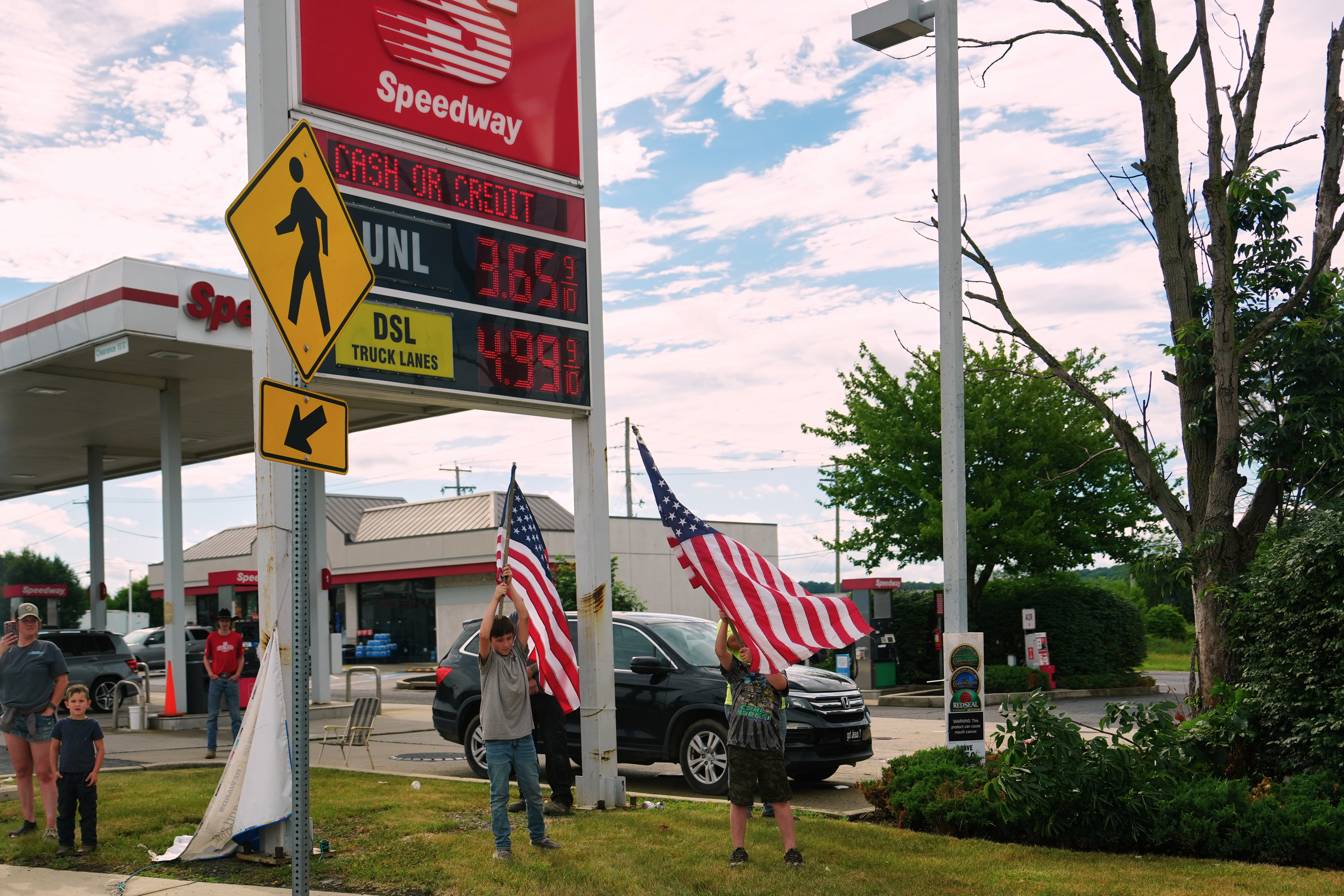 People hold flags in front of a gas station as President Donald Trump's motorcade passes by Tuesday, June 23, 2026, in Pennsylvania.