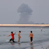 Three boys play in the shallow waters of the Strait of Hormuz as a plume of smoke rises from an explosion in the background off Bandar Abbas, Iran, July 13, 2026.