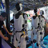 A worker reacts near a line of humanoid robots displayed at the World AI Conference in Shanghai, Friday, July 17, 2026.