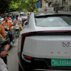 Two wheelers drive past an electric vehicle parked along a street in New Delhi, India, Monday, July 13, 2026.