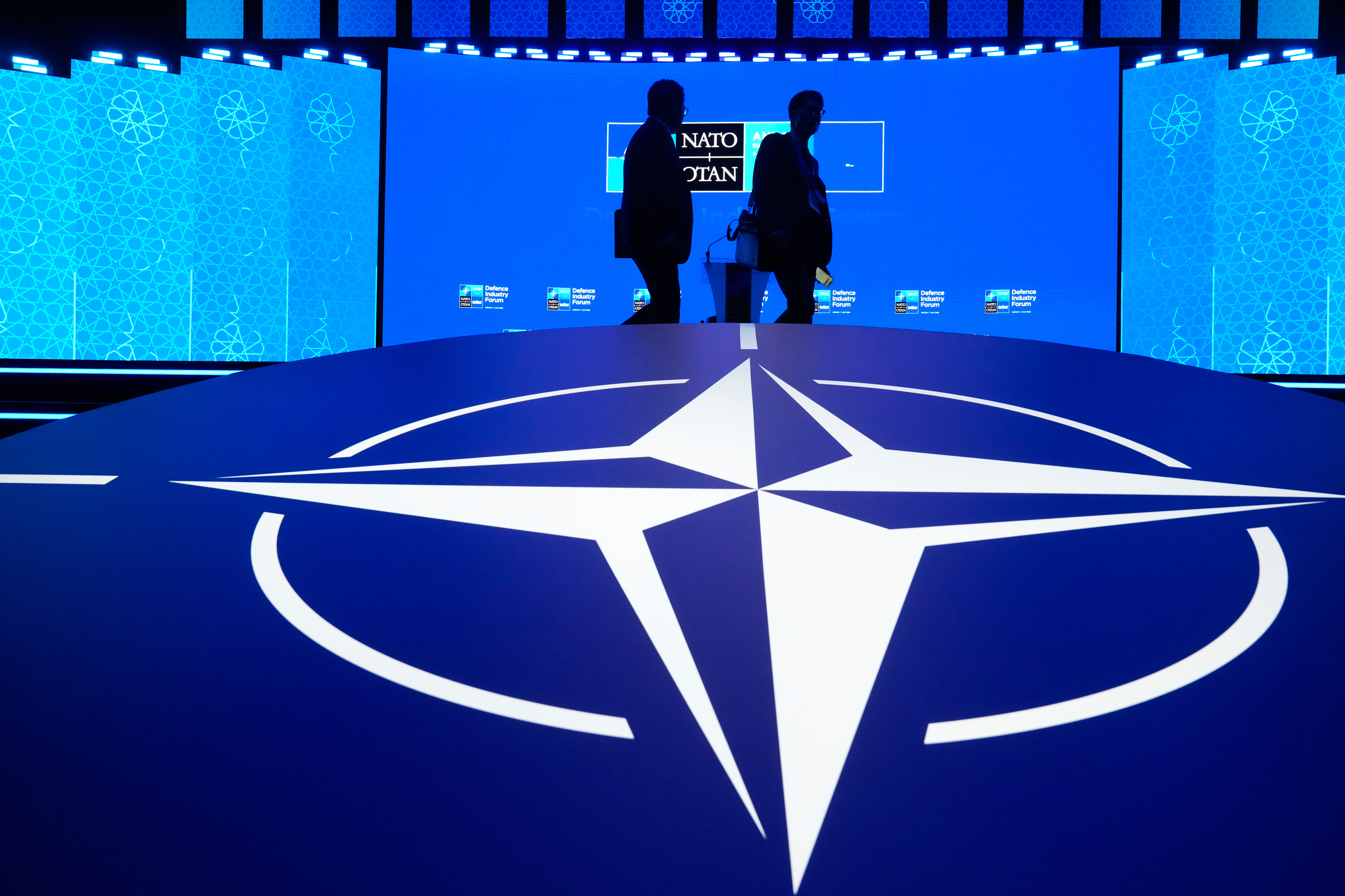 Two men walk past the NATO logo during the NATO Defense Industry Forum at the NATO summit in Ankara, Turkey, Tuesday, July 7, 2026.