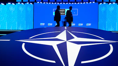 Two men walk past the NATO logo during the NATO Defense Industry Forum at the NATO summit in Ankara, Turkey, Tuesday, July 7, 2026.