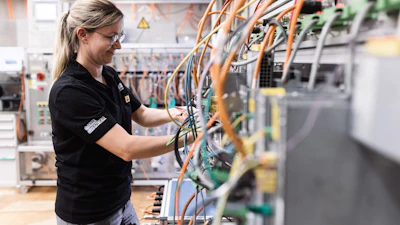 Female technician in safety glasses working on electrical panel with orange and blue wiring in industrial facility