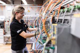 Female technician in safety glasses working on electrical panel with orange and blue wiring in industrial facility
